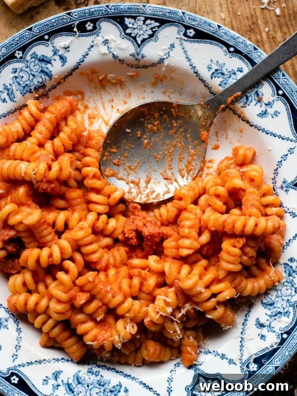 An overhead shot of creamy tomato pasta with Italian sausage in a blue patterned bowl with a serving spoon at the side.