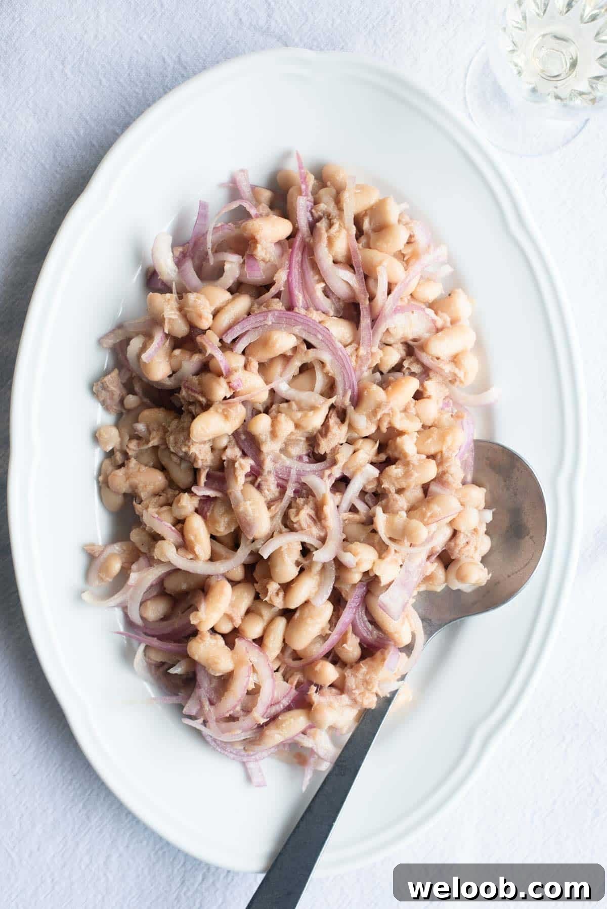An overhead shot of cannellini beans, tuna and onion on a white platter.