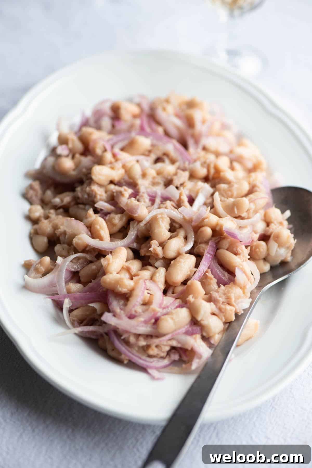 Cannellini beans, tuna and onion on a white plate with a serving spoon.