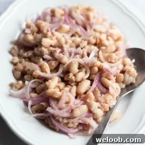 A cropped square image of a cannellini bean salad with tuna and onions on a white oval platter.