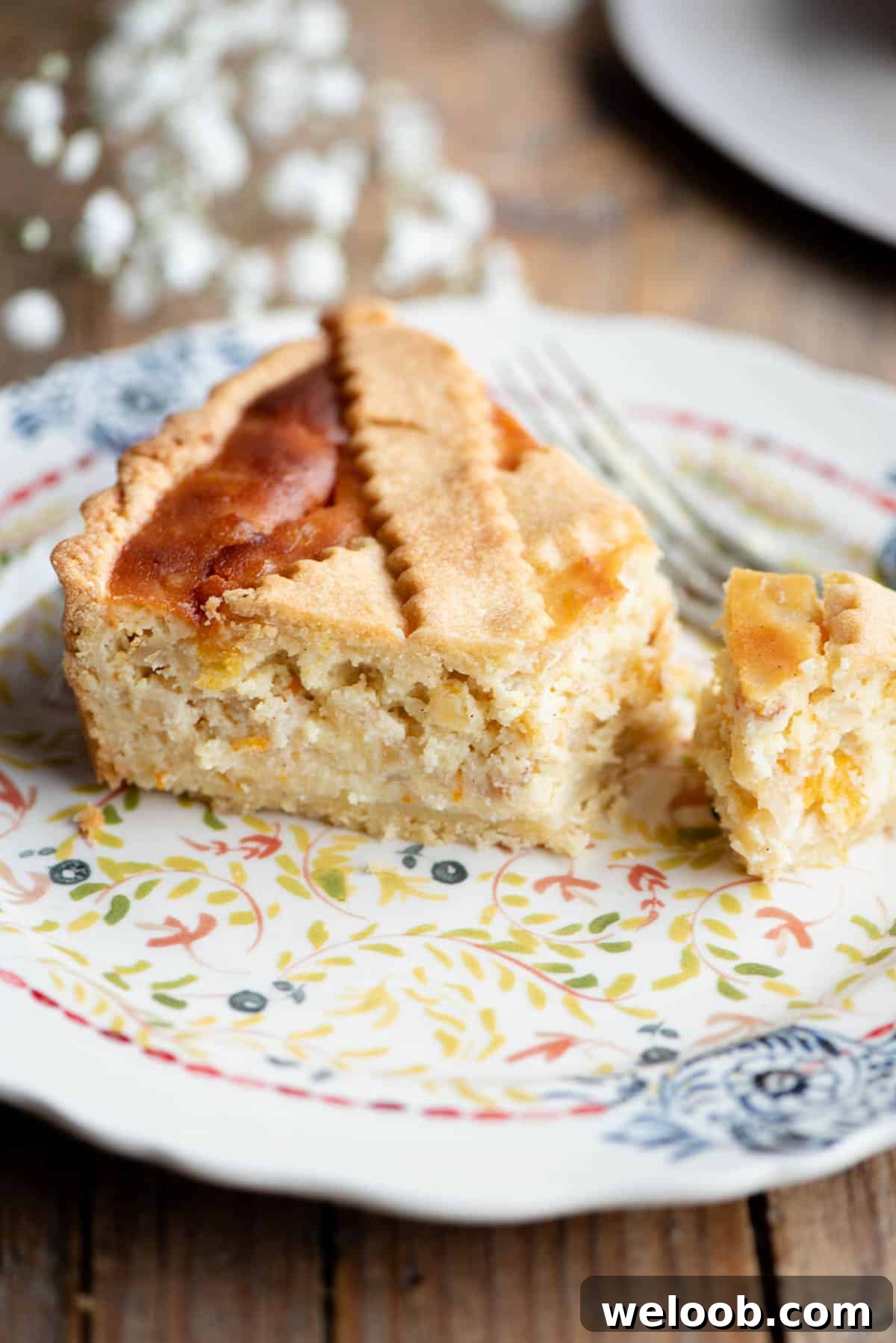 A slice of Pastiera Napoletana on a patterned plate with white flowers in the background.