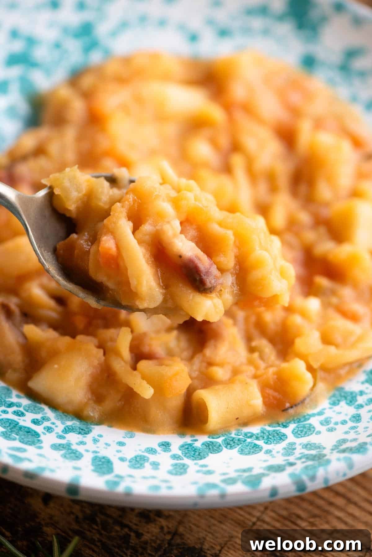 A close up of a spoonful of pasta and potatoes over a bowl.