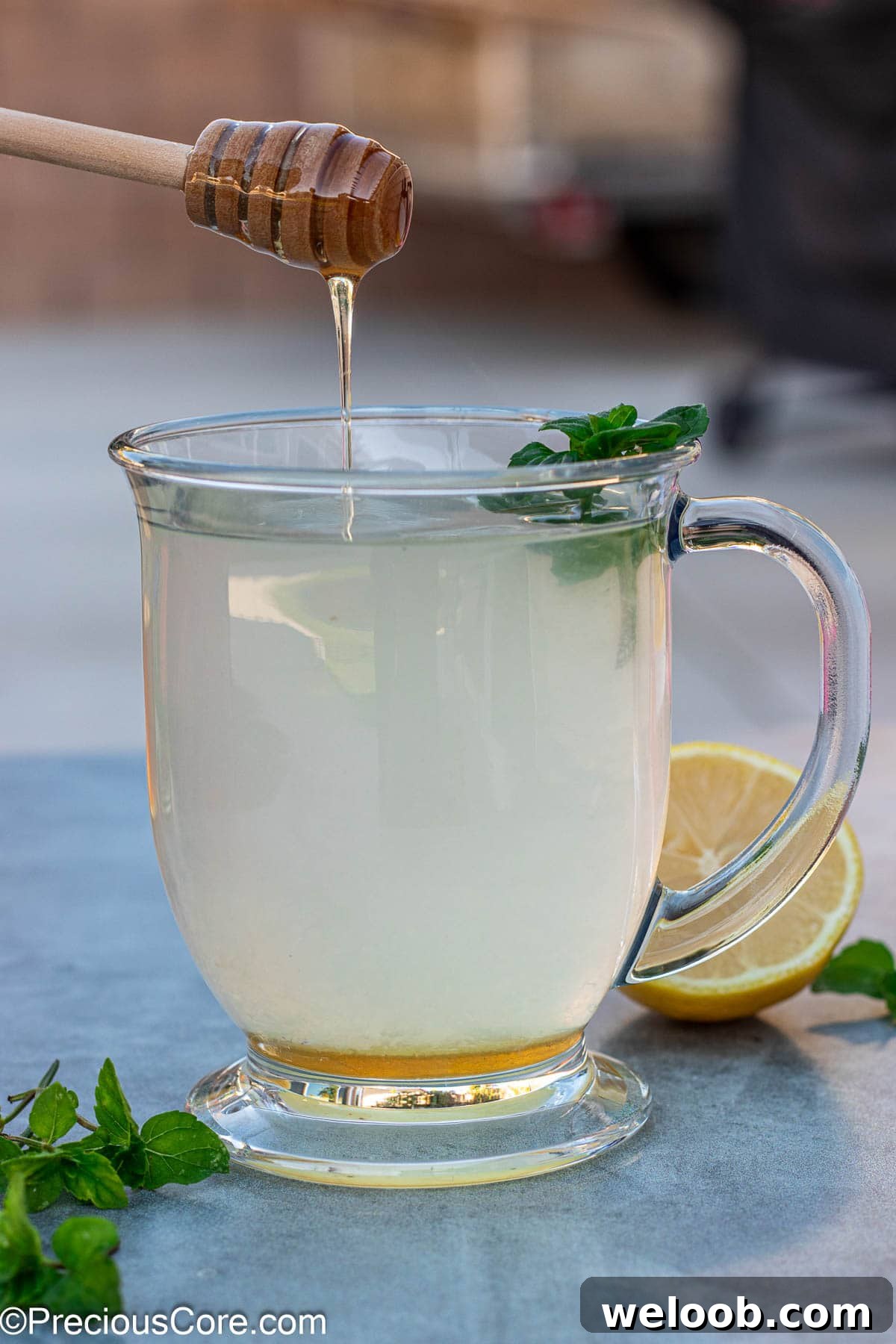 Honey dipper dripping honey into a cup of honey lemon tea.