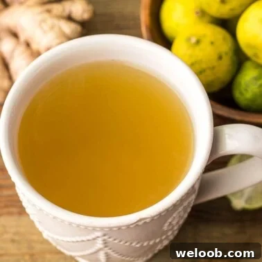 A mug of fresh ginger drink with some ginger and key limes on the side