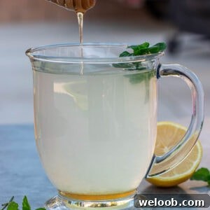 Honey dipper dripping honey into a cup of honey lemon tea.