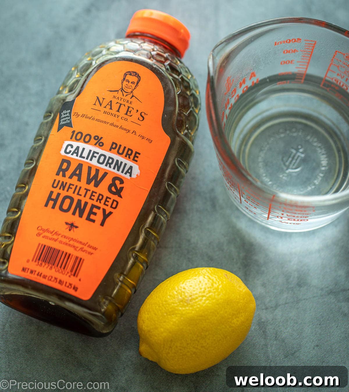 Container of honey, a lemon and water in a cup.