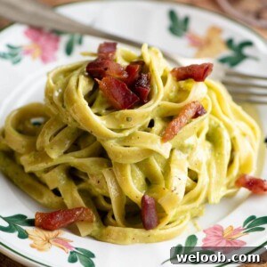 A cropped square image of pistachio pasta on a floral patterned plate topped with crispy guanciale (bacon).