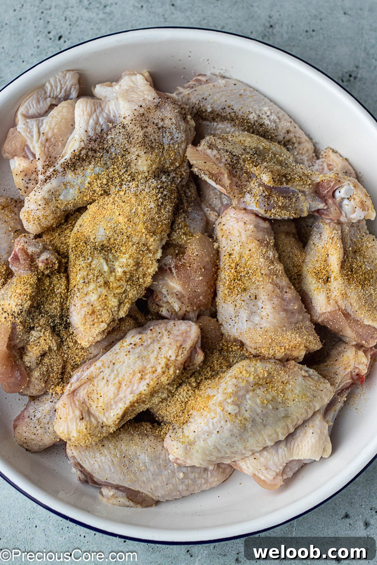 Chicken wings in a white bowl with powdered seasoning on top.