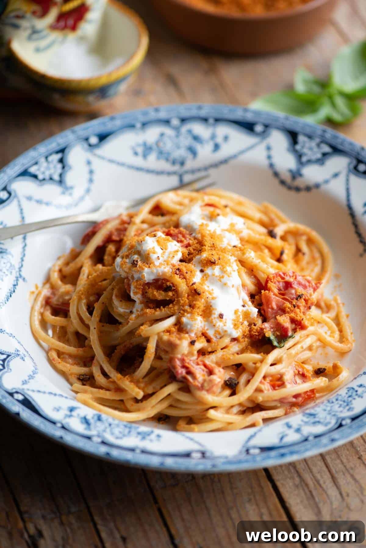 Roasted cherry tomato spaghetti in a blue bowl sitting on a wooden background.