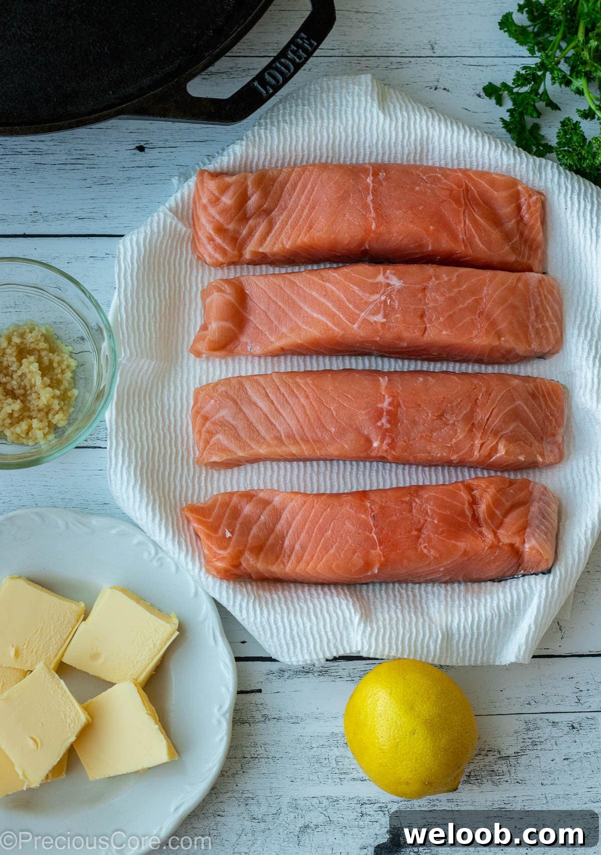 Pan-Seared Lemon Butter Salmon with Garlic and Herbs 3 Raw salmon, minced garlic, butter, and lemon on a board.