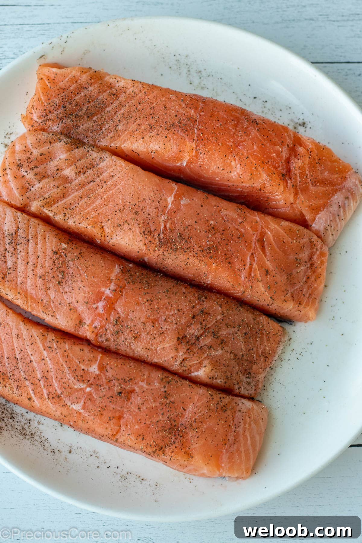 Pan-Seared Lemon Butter Salmon with Garlic and Herbs 4 4 salmon fillet on a white plate, seasoned with salt and pepper.