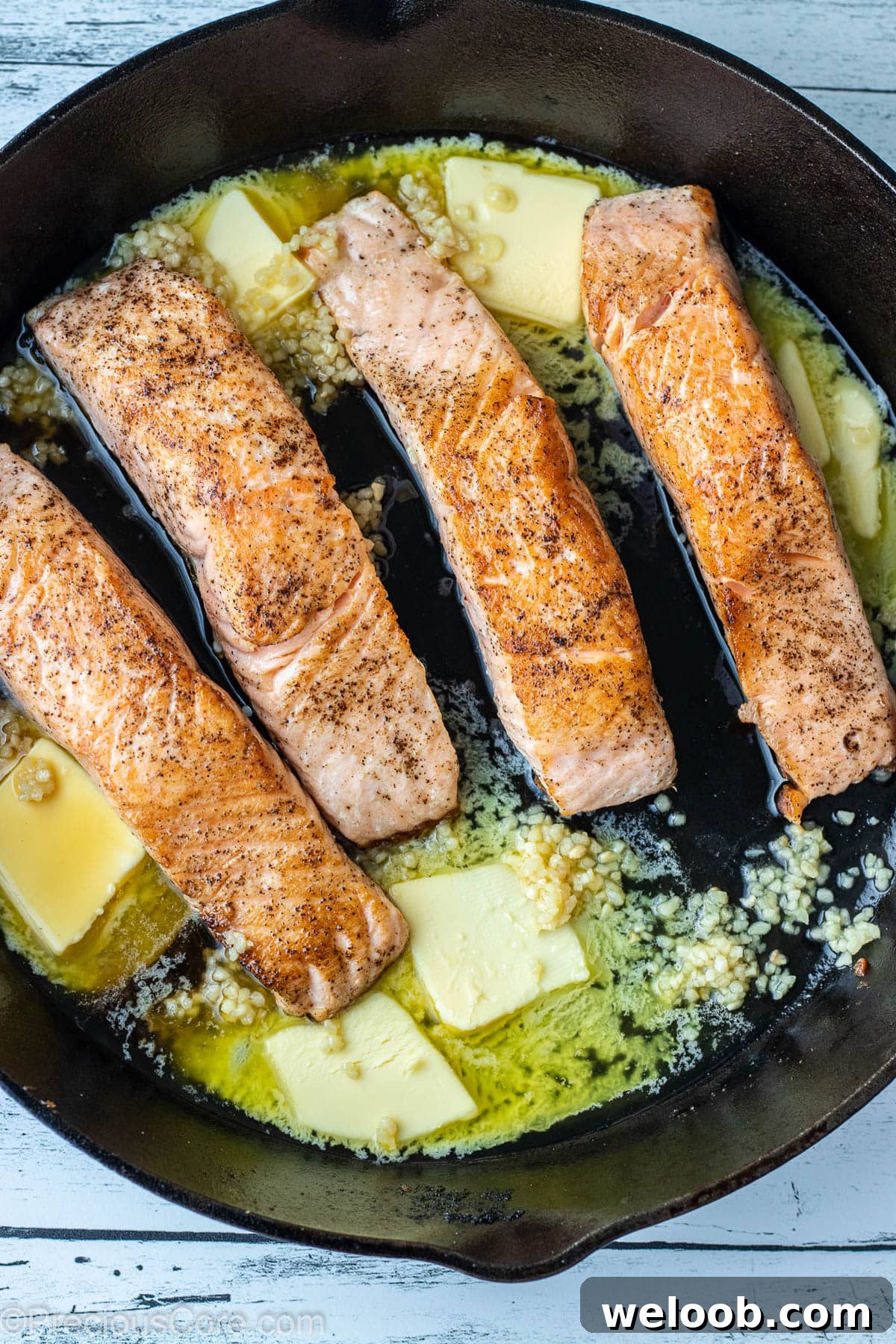 Pan-Seared Lemon Butter Salmon with Garlic and Herbs 6 Butter and minced garlic in a cast iron skillet with seared salmon.