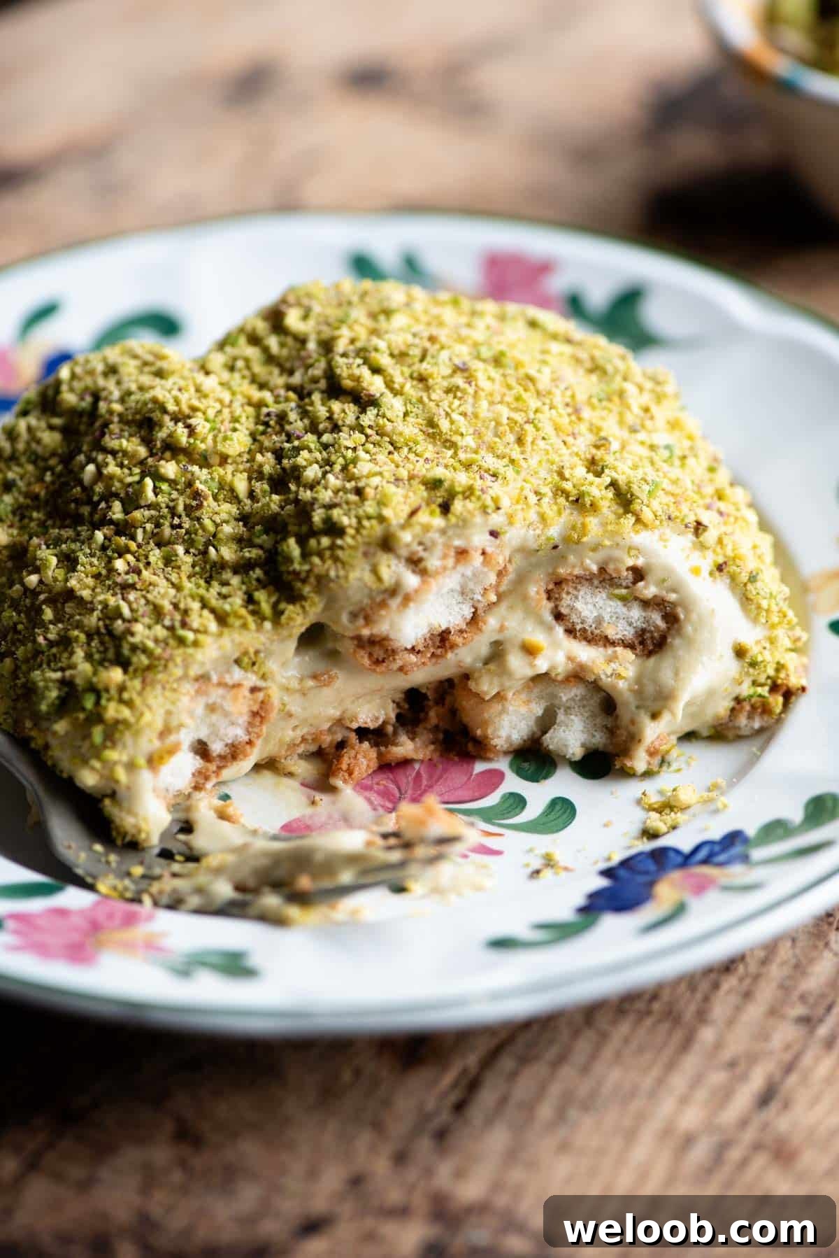 A close up of a piece of pistachio tiramisu on a plate sitting on a wooden table.