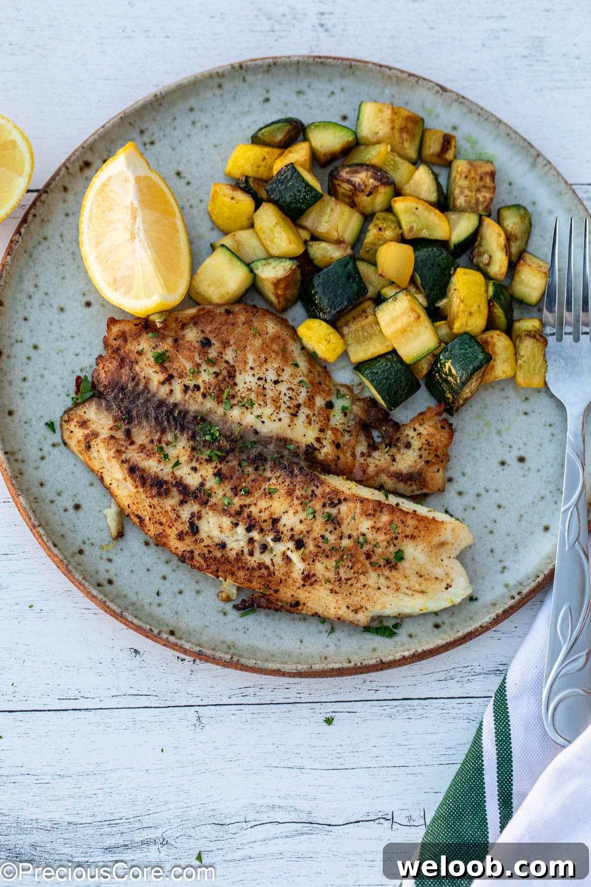 Lemon pepper tilapia on a plate with sautéed zucchini.