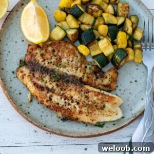 Lemon pepper tilapia on a plate with sautéed zucchini.