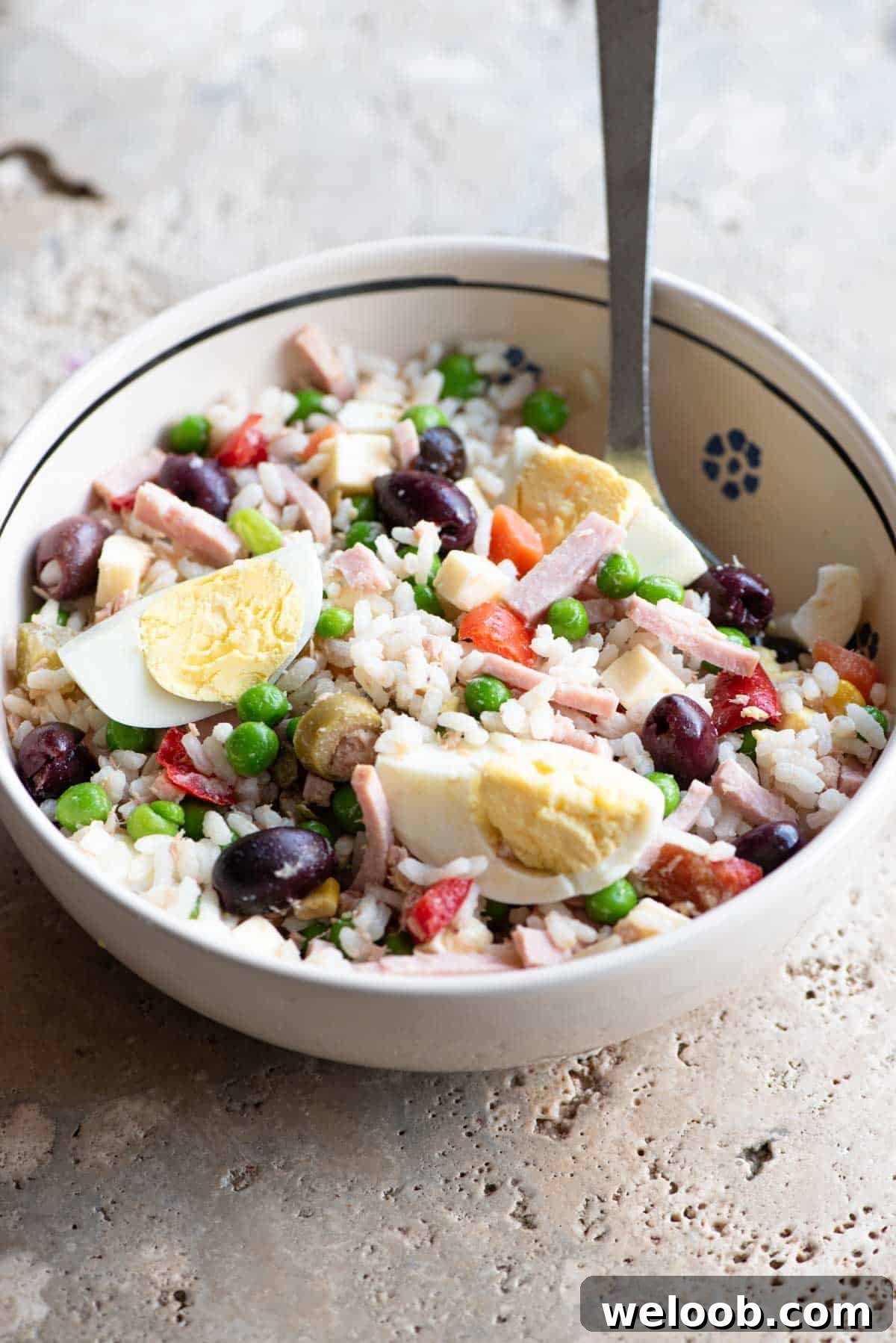 A traditional Italian rice salad in a bowl sitting on a rustic stone work top.