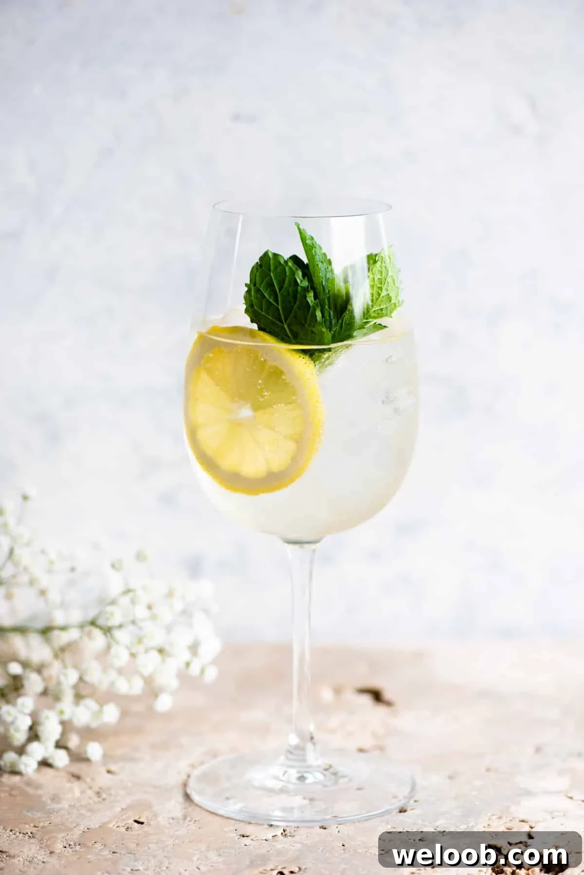 A Hugo spritz cocktail on a light coloured worktop with lemon and mint.
