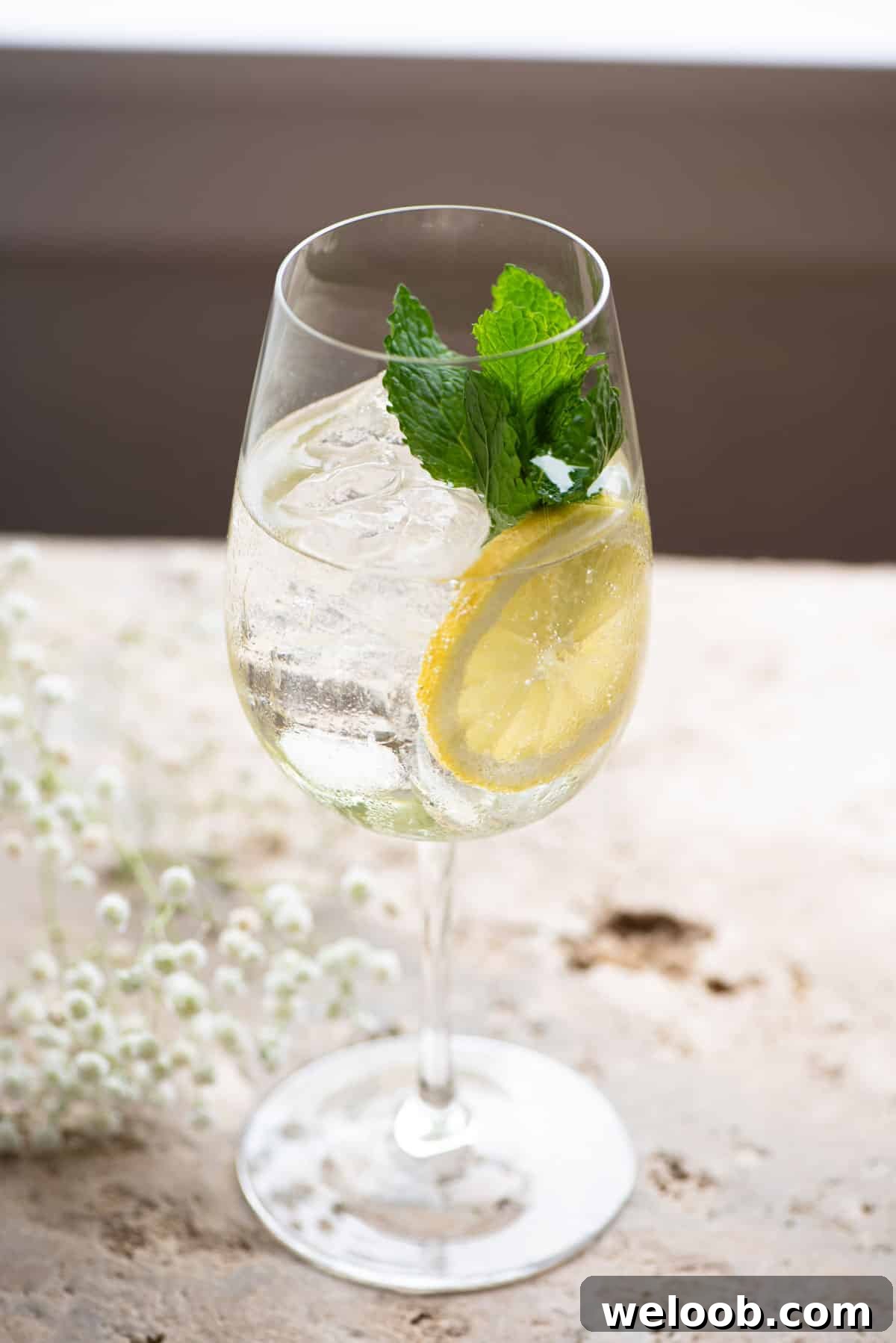 A hugo spritz cocktail on a stone worktop garnished with lemon and mint leaves.