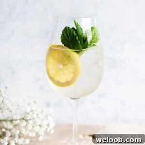 A close up cropped image of a Hugo Spritz on a light work surface garnished with lemon and mint.