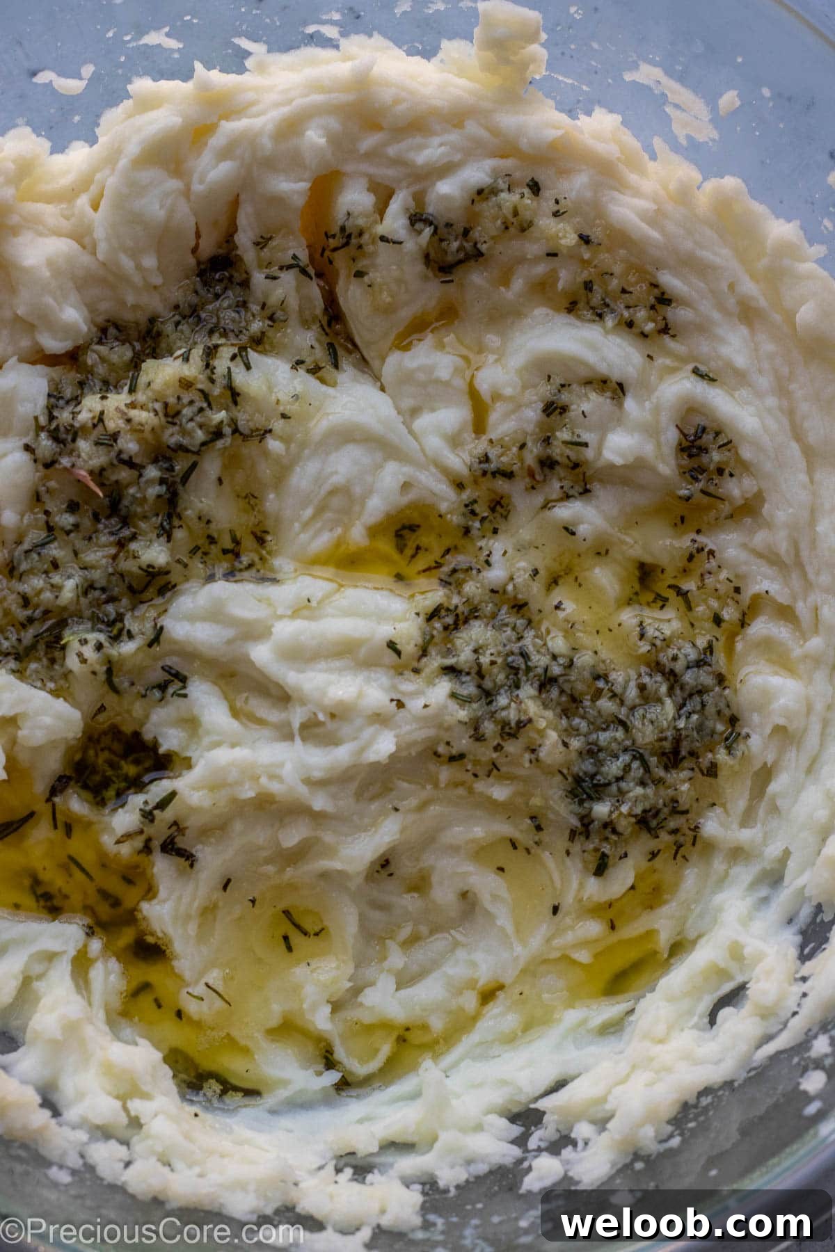 Melted butter and minced garlic and rosemary over mashed potatoes in a bowl.