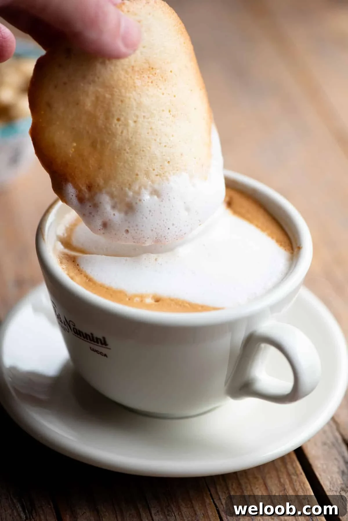 A close up of an Italian cookie called Tegola Valdostana getting dunked into a cappuccino.
