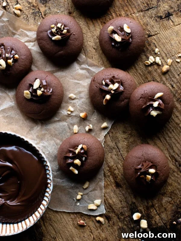 An overhead shot of Nutella cookies on a wooden surface with a ramekin of Nutella at the side and chopped hazelnuts.