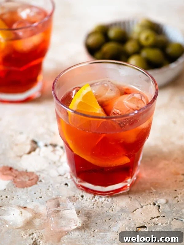An Americano cocktail on a marble work surface with olives in the background