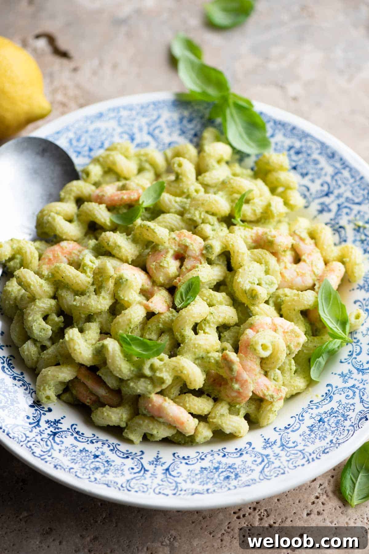 Zucchini shrimp pasta salad in a blue and white bowl topped with basil leaves.