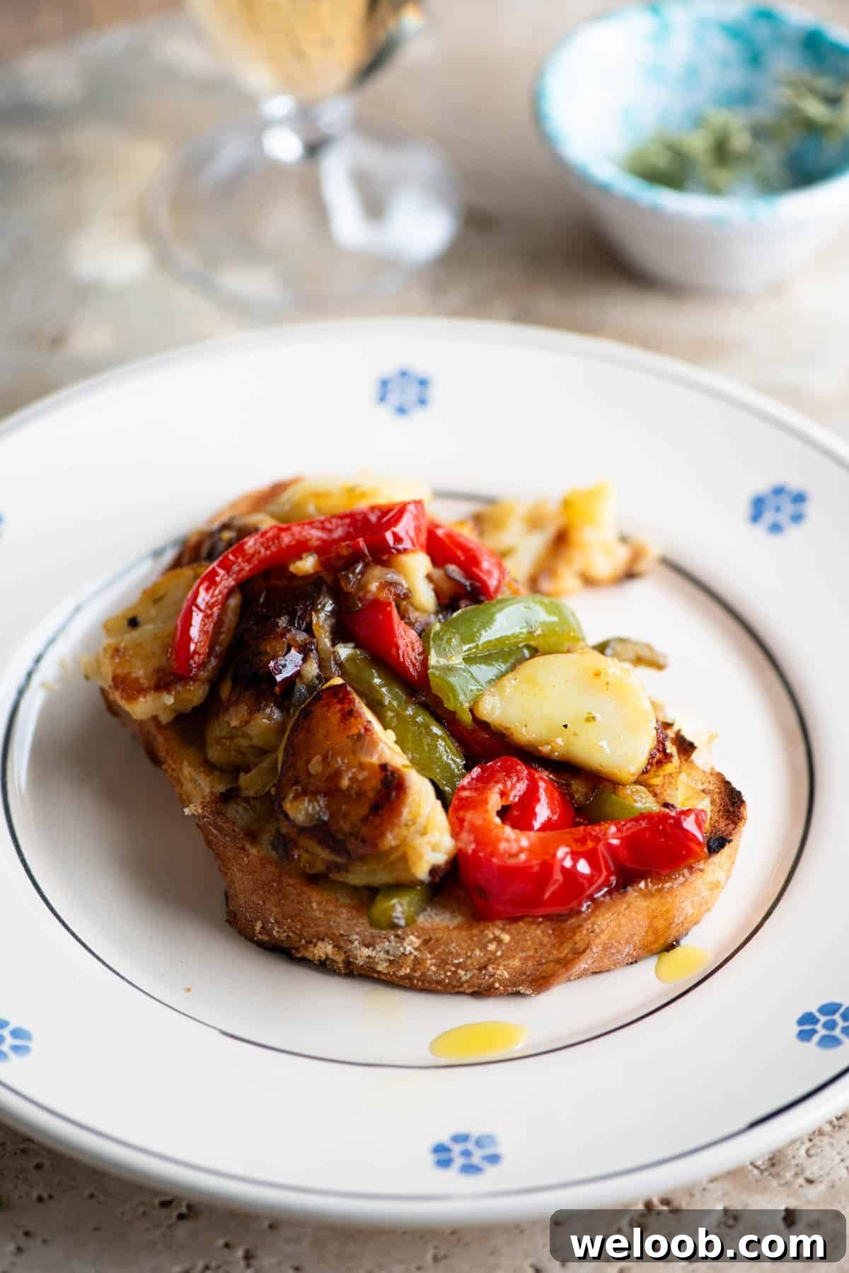 A side shot of peppers and potatoes on a slice of crusty bread sitting on a plate.