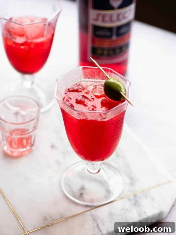 A select spritz in a glass topped with an olive.