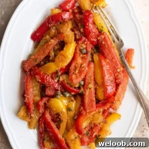 A cropped image of sauteed peppers mixed with capers and breadcrumbs on a white oval serving plate.