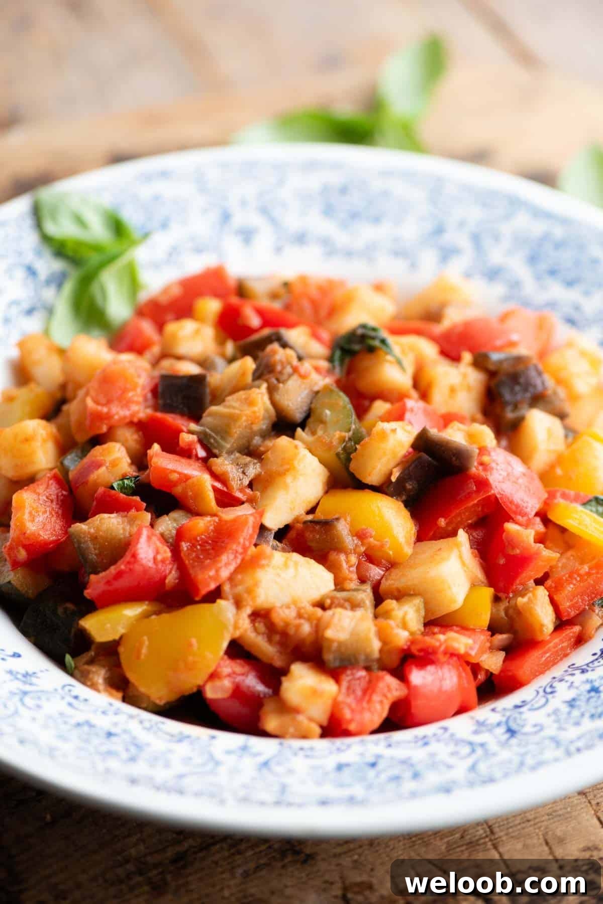 A side shot of Ciambotta vegetable stew in a blue and white bowl sitting on a wooden board.