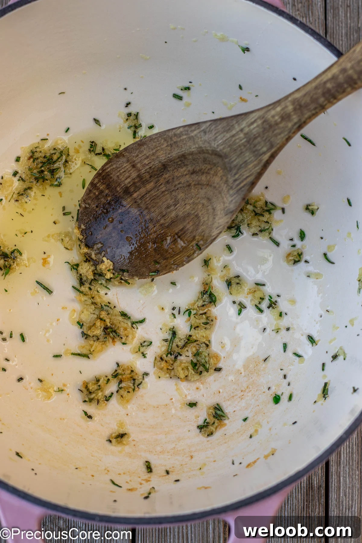 Garlic and fresh herbs sauteeing in olive oil in a cast iron enamel pot.
