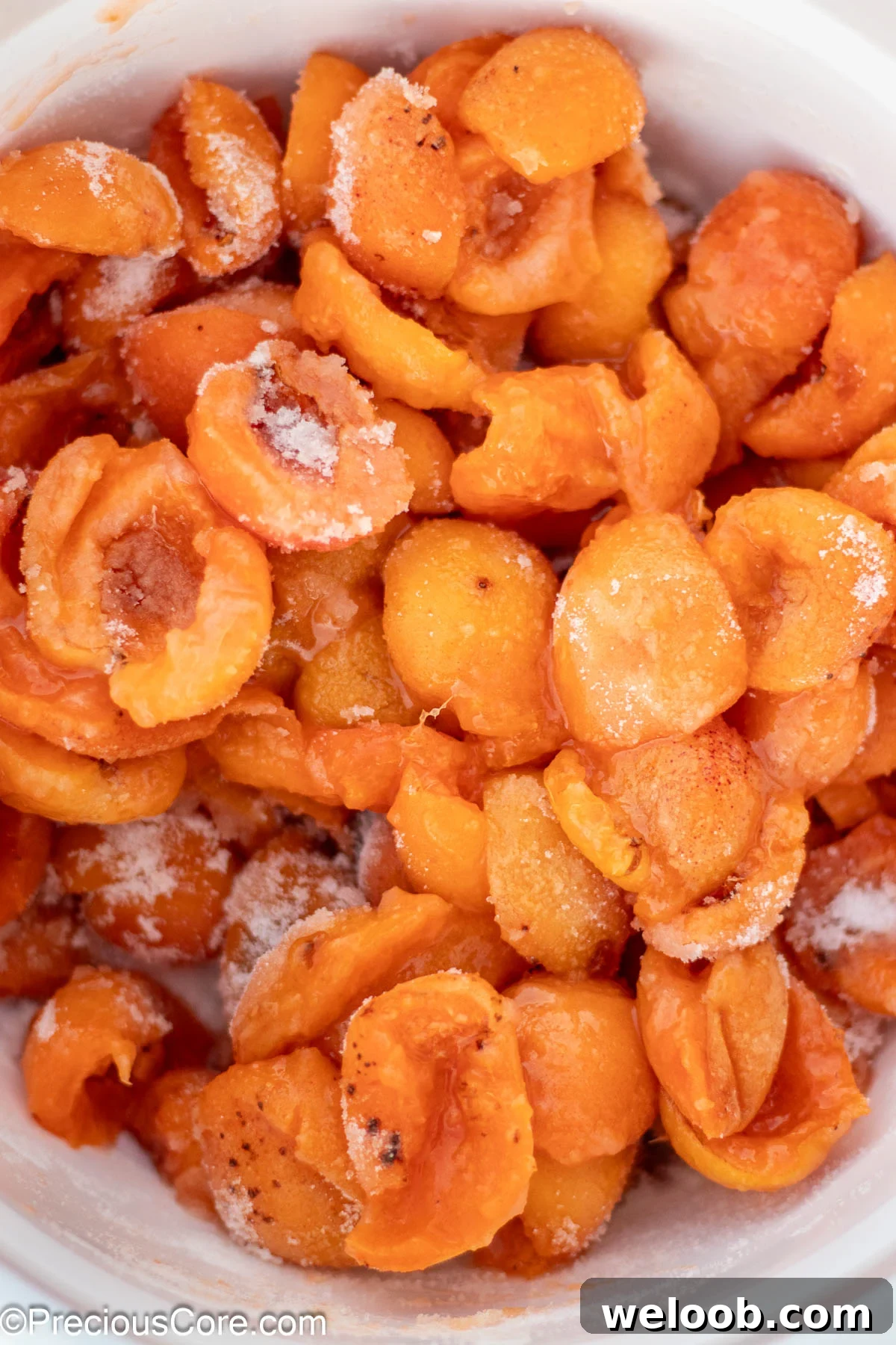 Halved apricots mixed with granulated sugar in a white bowl.