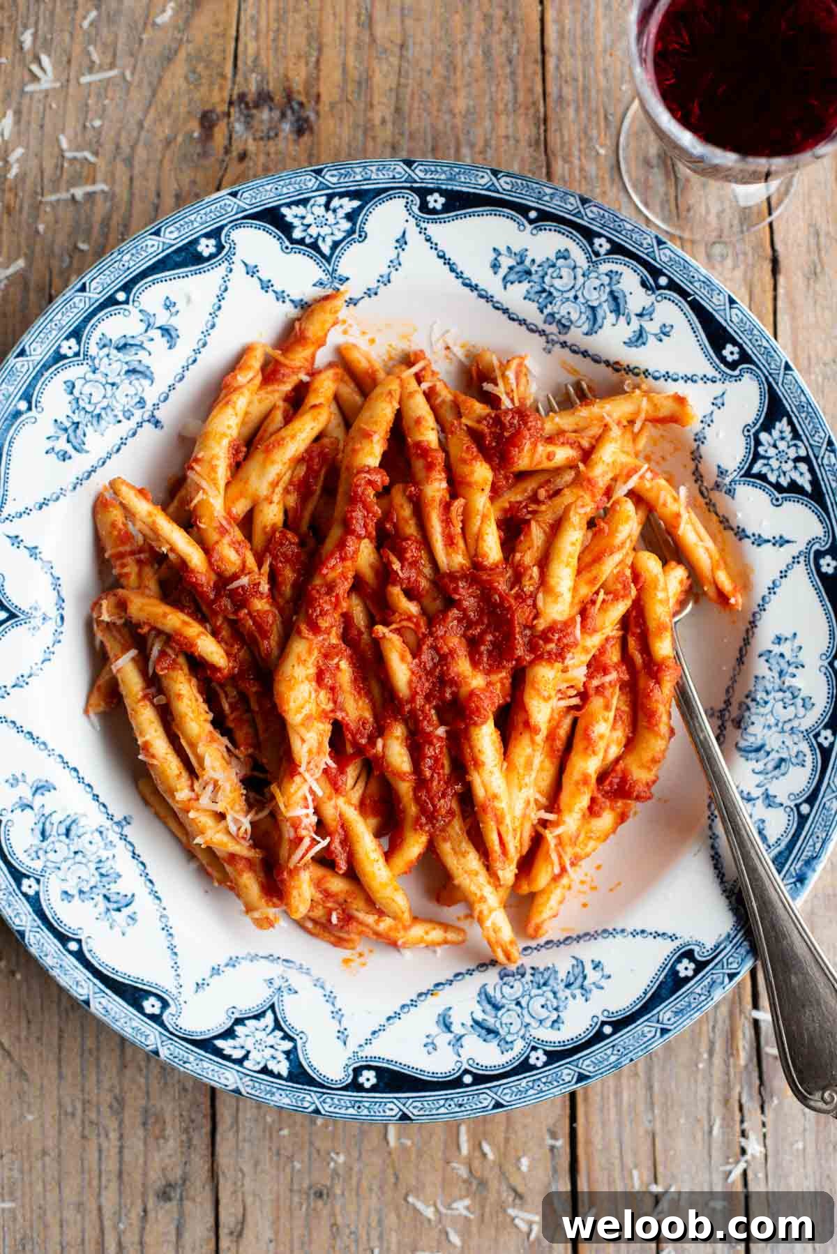 An overhead shot of spicy Nduja pasta (Fileja) in a blue and white bowl with a fork, the background is rustic wood.