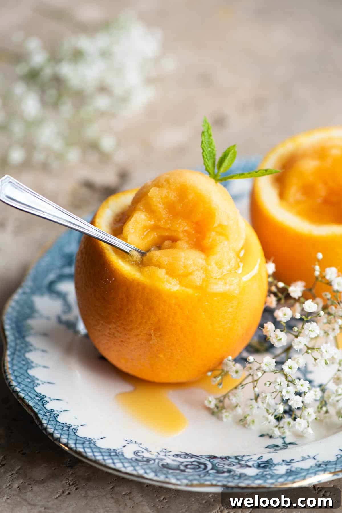 A close up of orange sorbet served inside an orange sitting on a blue plate with flowers at the side.