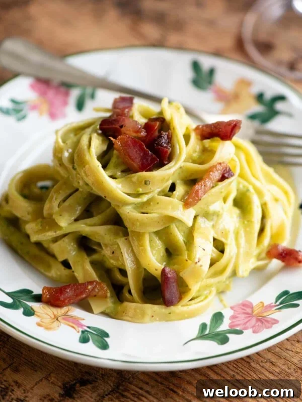 Creamy pistachio pasta on a floral patterned plate topped with guanciale. The background is wooden.