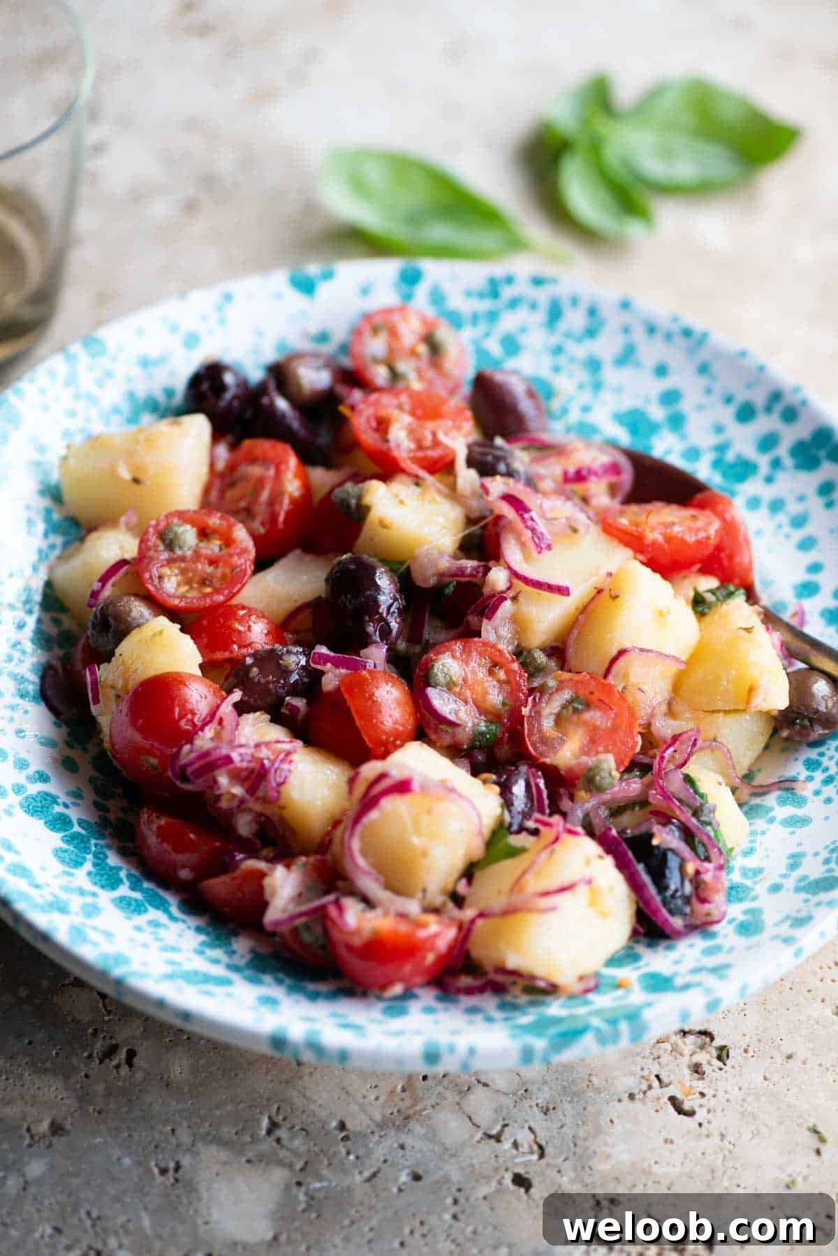 A Sicilian potato salad with olives, tomatoes and onions in a blue and white bowl.
