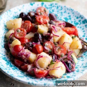 A close up cropped image of a Sicilian potato salad in a blue bowl with olives, onions and tomatoes.