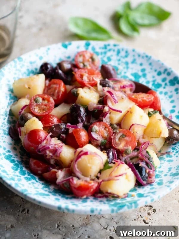 A Sicilian potato salad with olives, tomatoes and onions in a blue and white bowl.