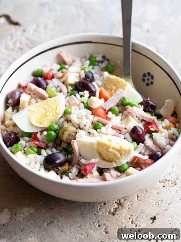 A traditional Italian rice salad in a bowl sitting on a rustic stone work top.