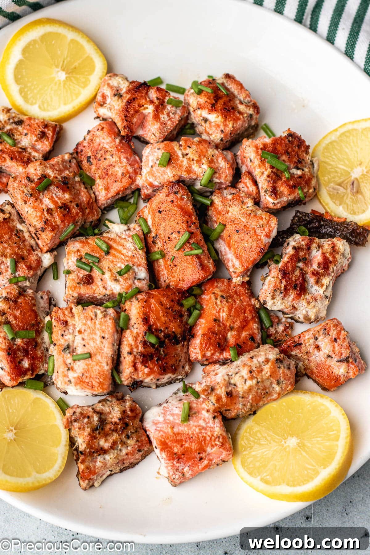Bites of salmon on a white plate garnished with lemon slices.
