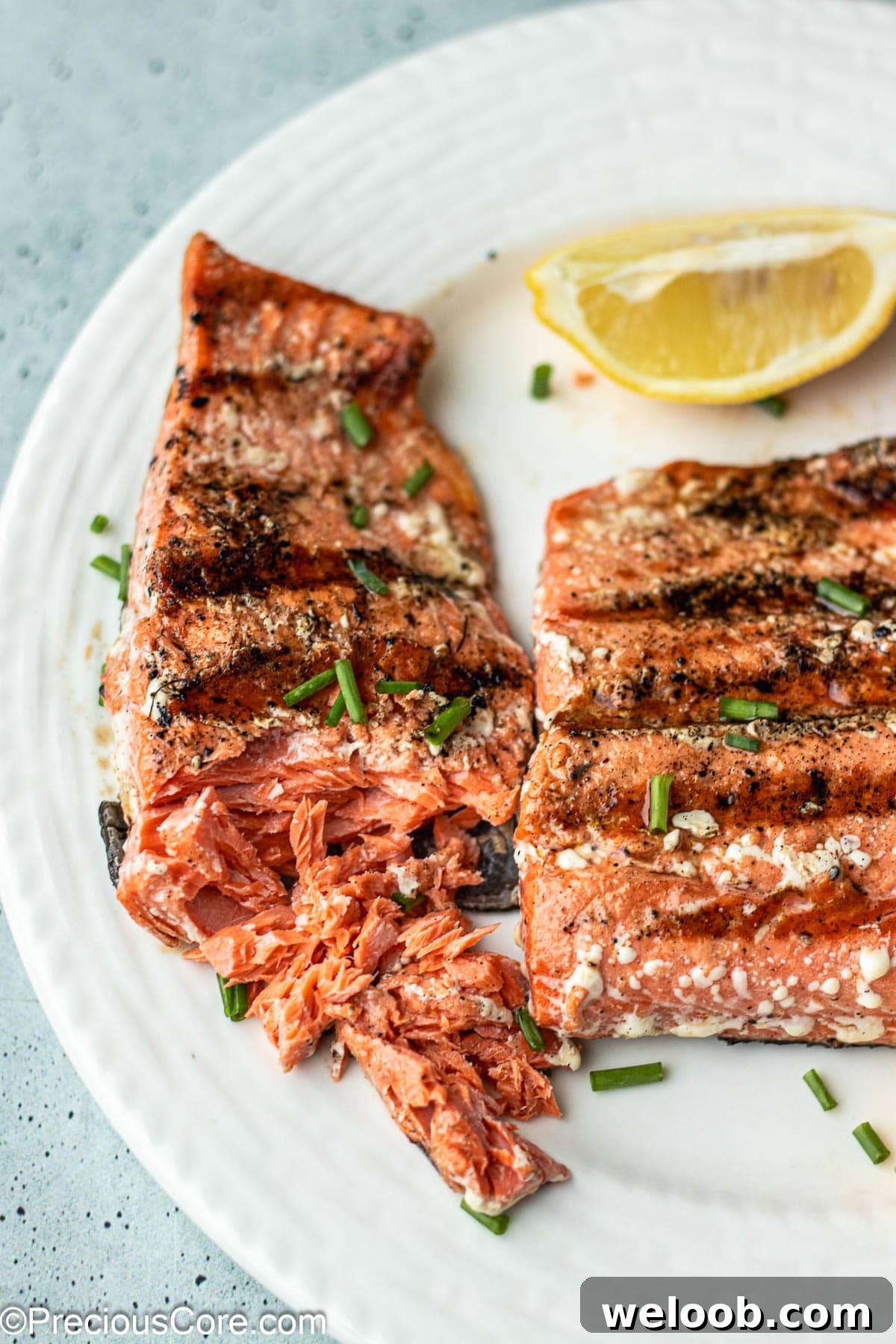 2 grilled salmon on a plate with one flaked with a fork.