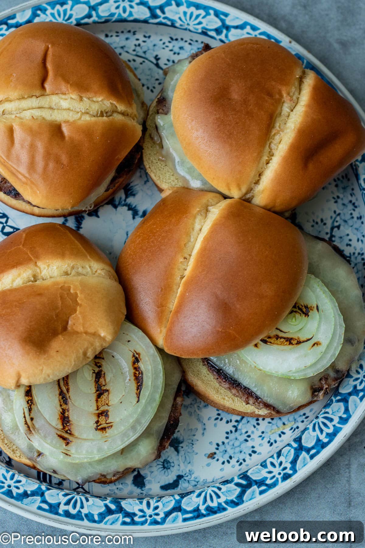 4 burgers with grilled onions on a round platter.