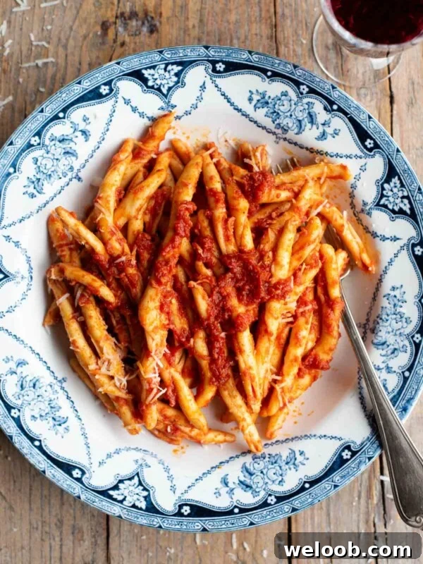An overhead shot of spicy Nduja pasta (Fileja) in a blue and white bowl with a fork, the background is rustic wood.