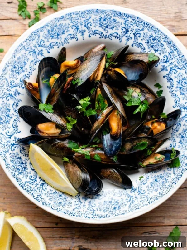 An overhead shot of peppered mussels in a blue bowl with fresh parsley and lemon.