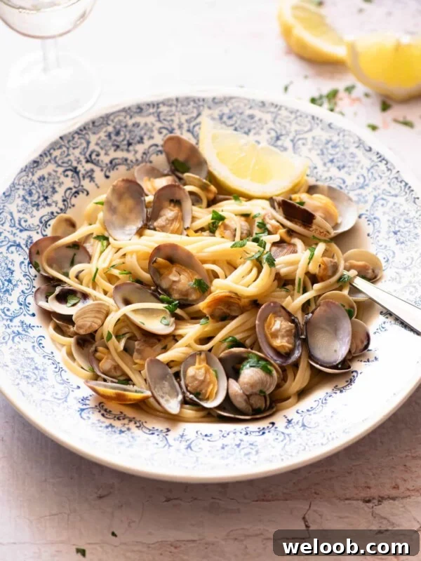 Linguine alle Vongole in a blue bowl with a slice of lemon at the side.