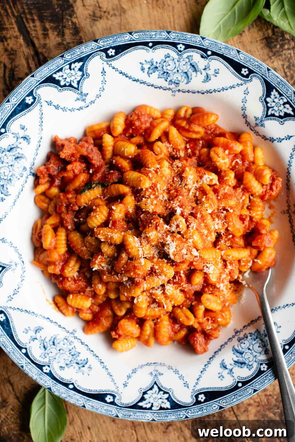 An overhead shot of a Sardinian sausage ragu (Malloreddus alla Campidanese) in a blue and white bowl on a rustic wooden background.