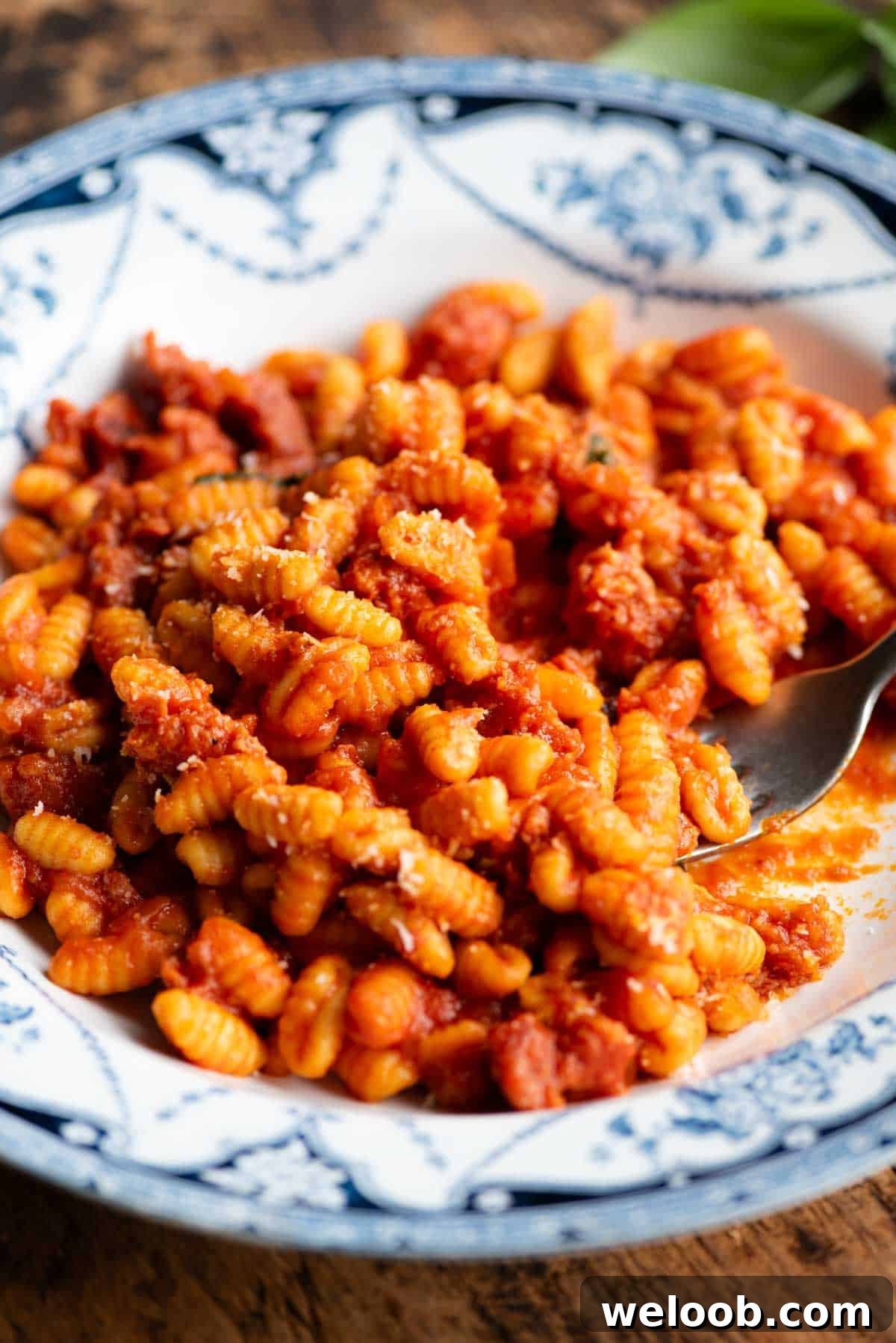 A close up side shot of a Sardinian sausage pasta in a blue and white bowl with a fork.