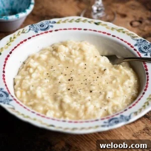 A close up cropped image of risotto alla Valdostana in a bowl ona. wooden surface.
